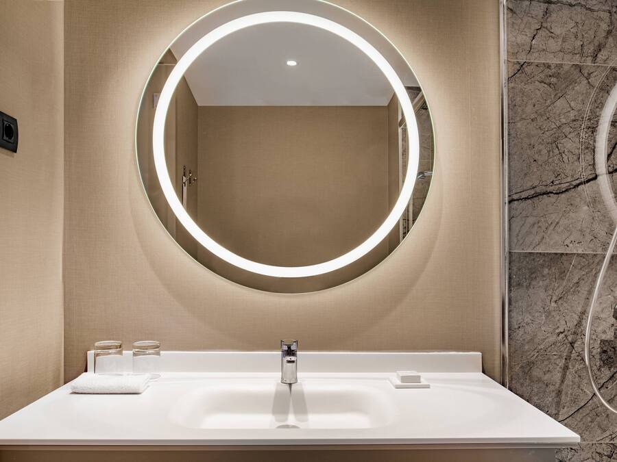 Une salle de bain moderne avec un grand miroir, un lavabo blanc et un espace douche.