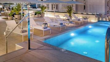 An outdoor swimming pool with lounge chairs and umbrellas, surrounded by potted plants and a bar area.