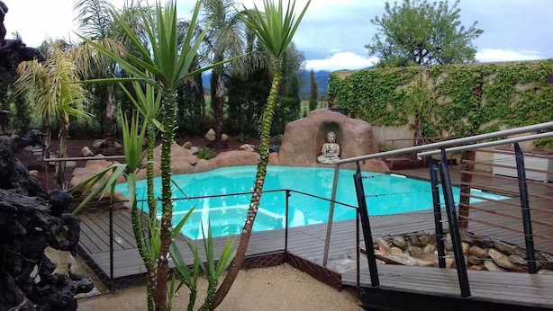 Piscina con una estatua de Buda al fondo, rodeada de vegetación y un paisaje rocoso.