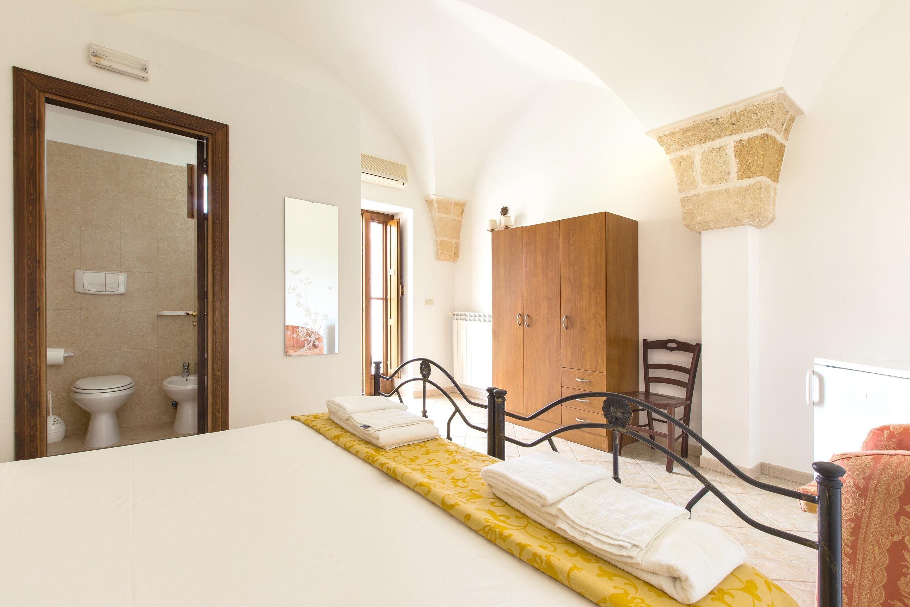 Un dormitorio con cama, armario de madera, baño con inodoro y bidé, y un arco de piedra.