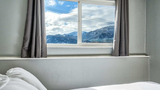 Ein Zimmer mit einem Bett, einem fenster mit Vorhängen und Blick auf Berge.
