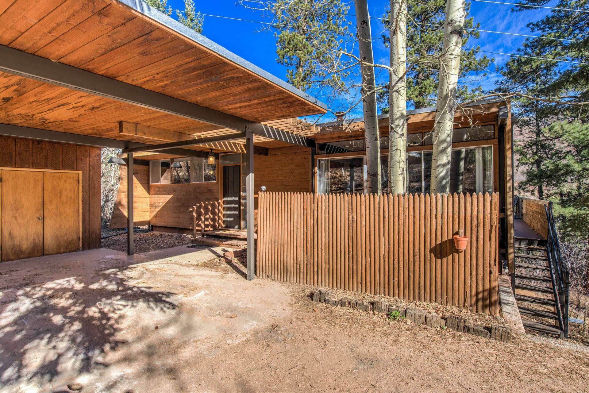 A wooden cabin with a covered porch, a fenced yard, and a view of trees.