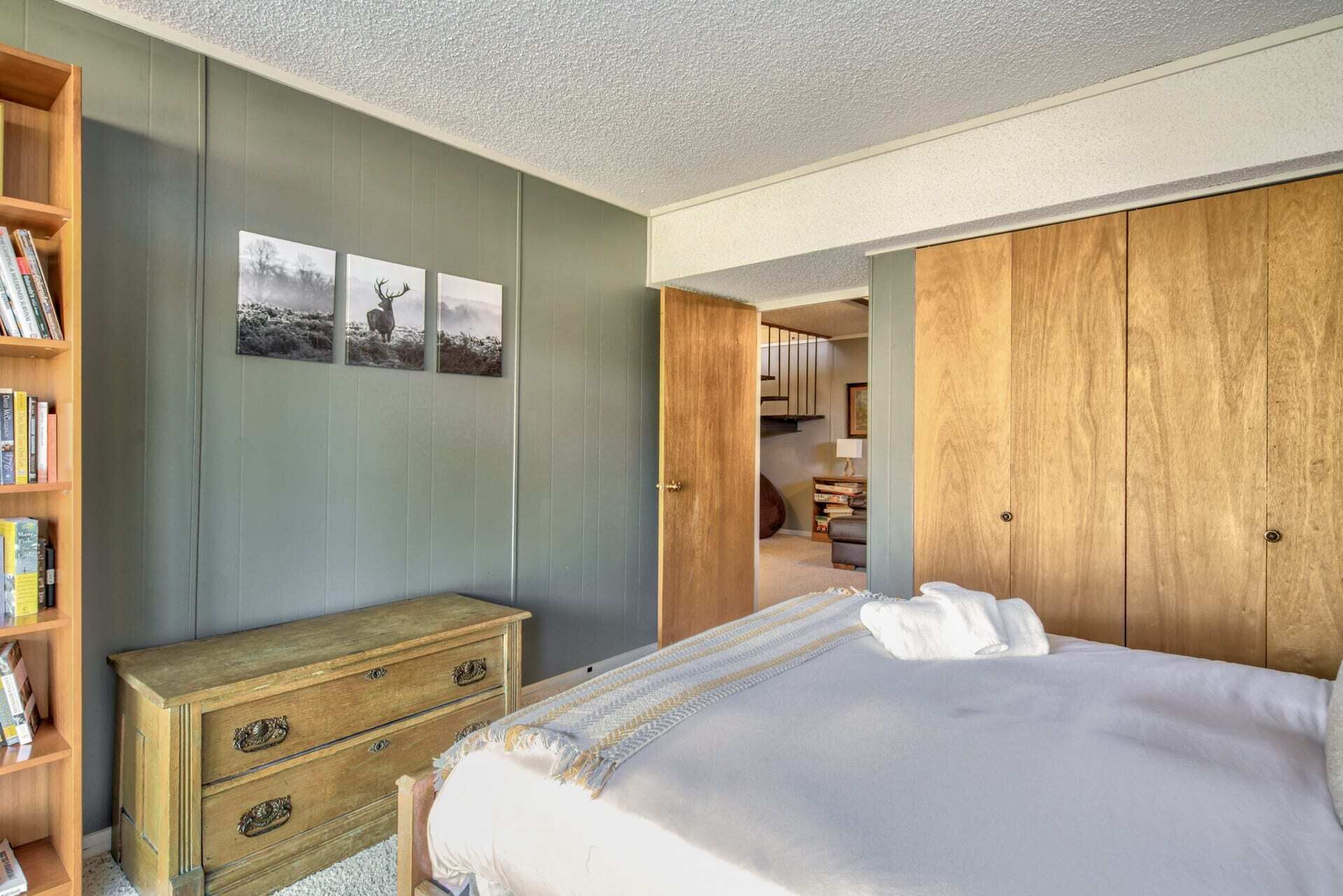 A bedroom with a bed, a wooden dresser, a bookshelf, and a wardrobe.
