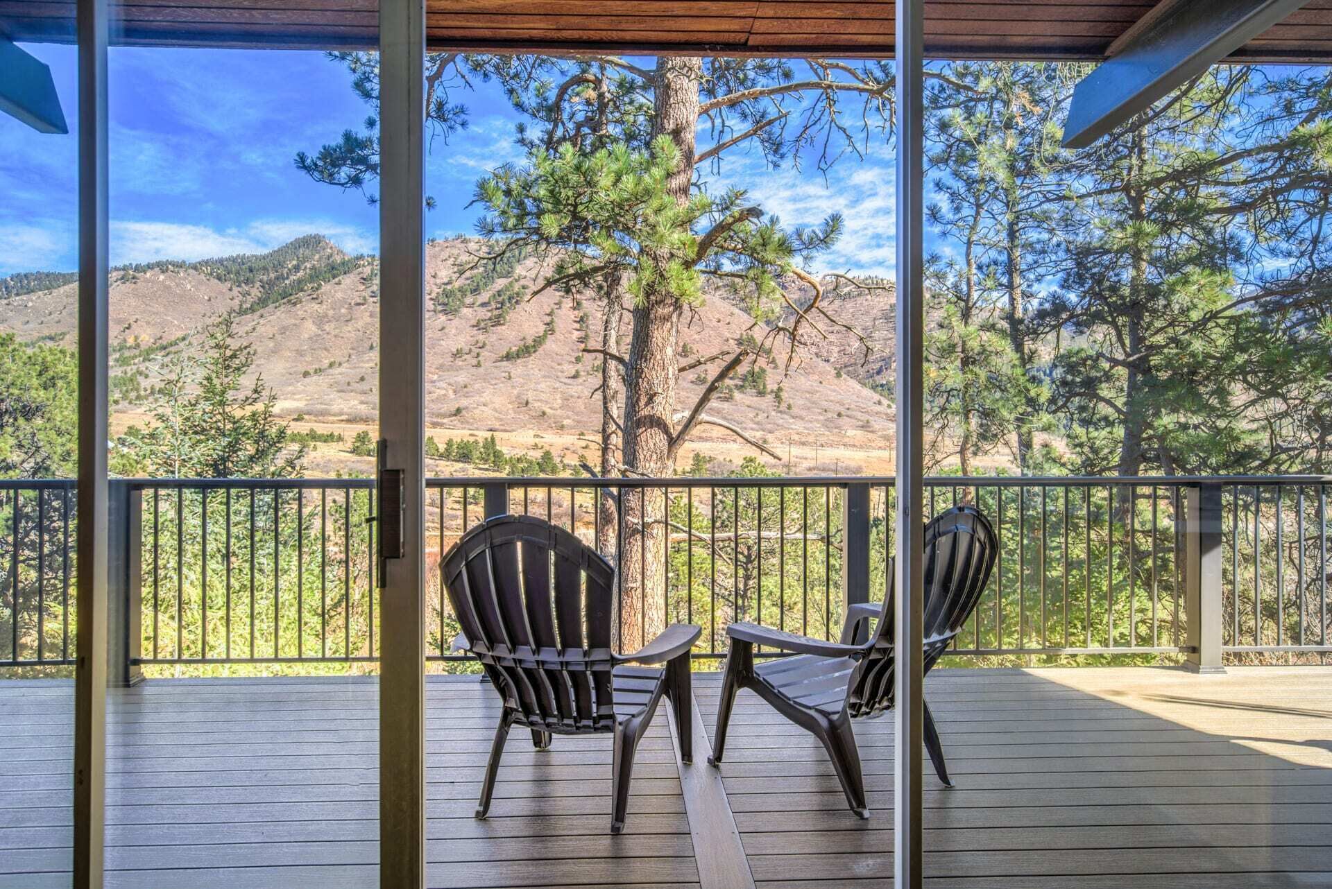 A covered outdoor deck with two Adirondack chairs facing a mountainous landscape.