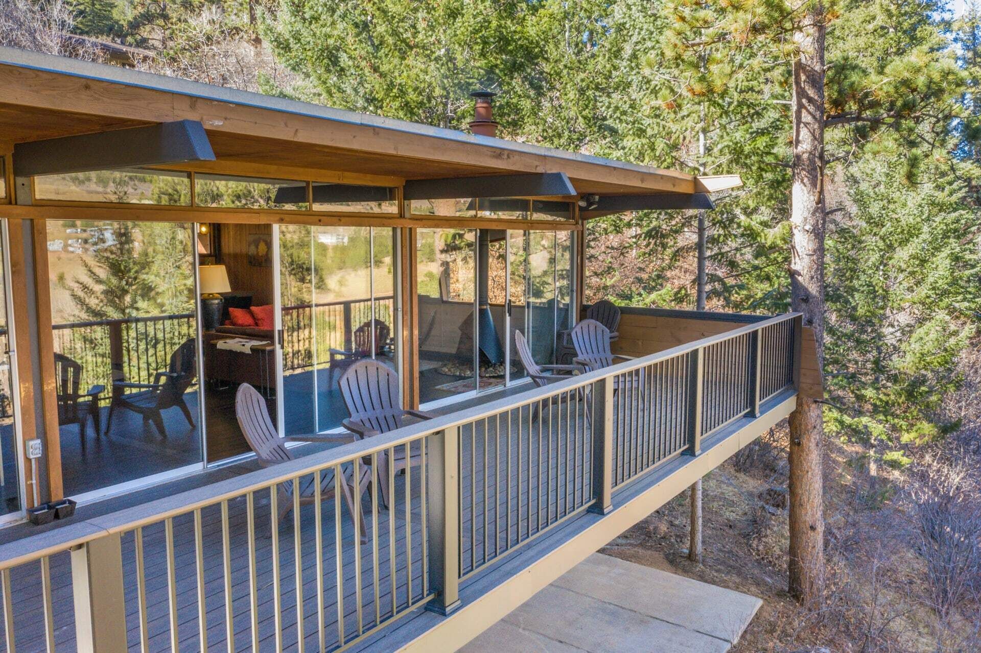 A wooden deck with chairs and a table, overlooking a forested area.