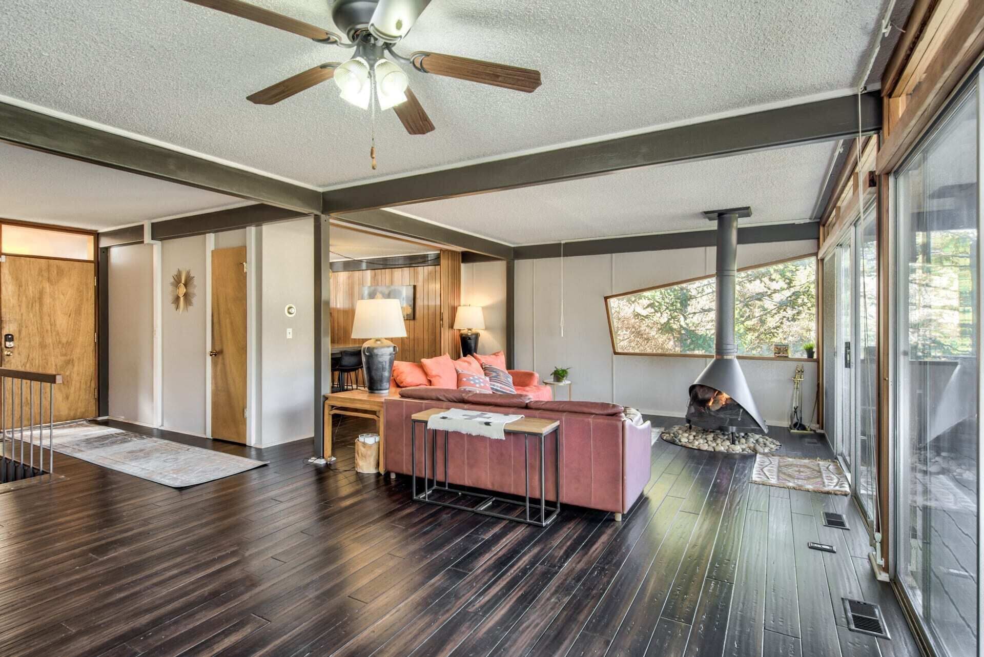 Una sala de estar moderna con chimenea, piso de madera y ventilador de techo.