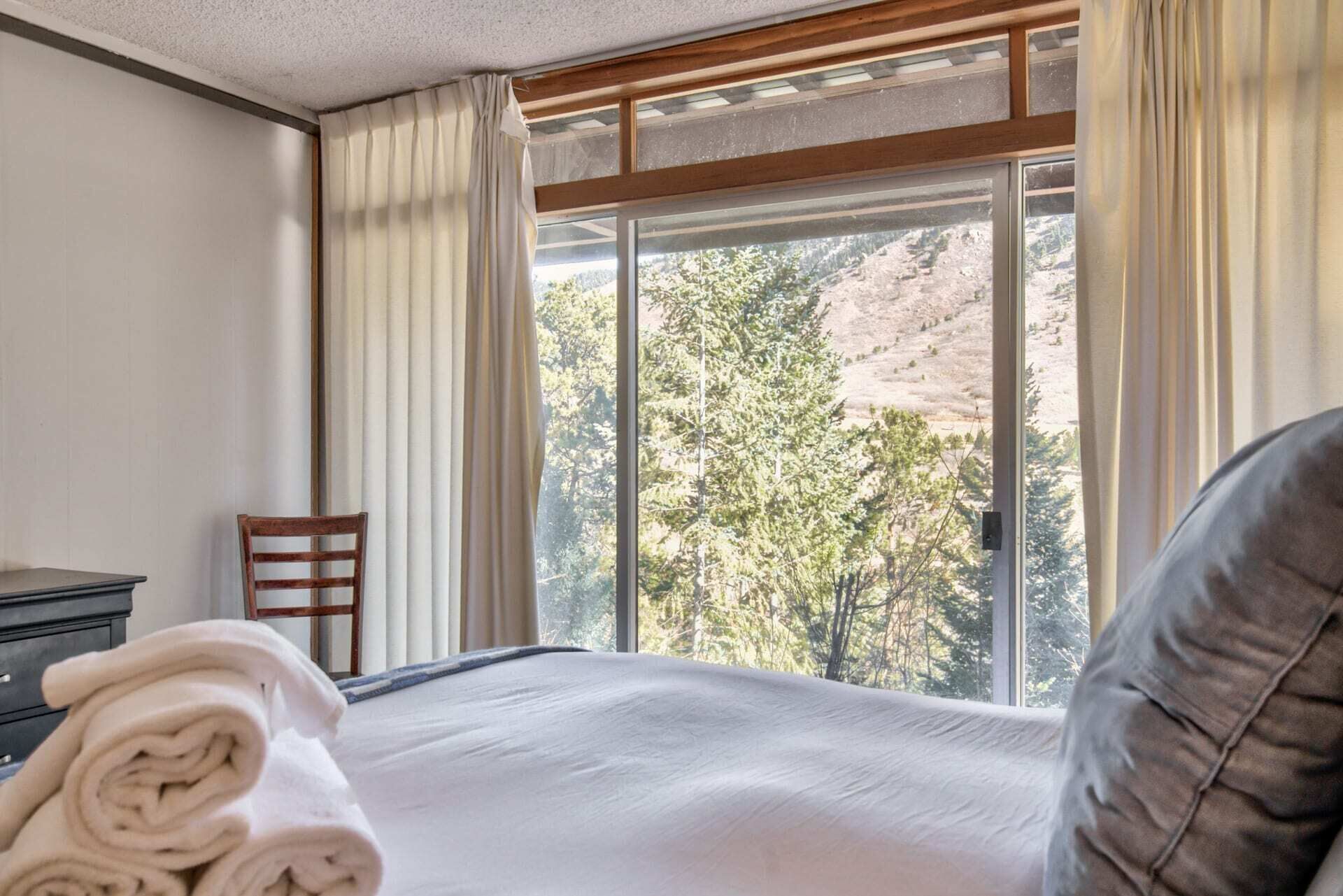 A hotel room with a large window, a bed, a chair, and a neatly folded towel.