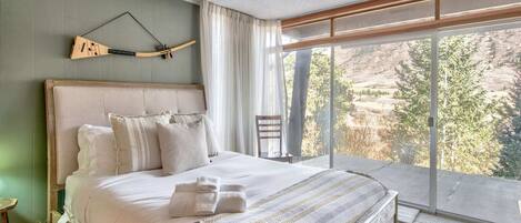 Un dormitorio con una cama grande, un cabecero de madera, vistas al exterior a través de amplias ventanas y una guitarra colgada en la pared.