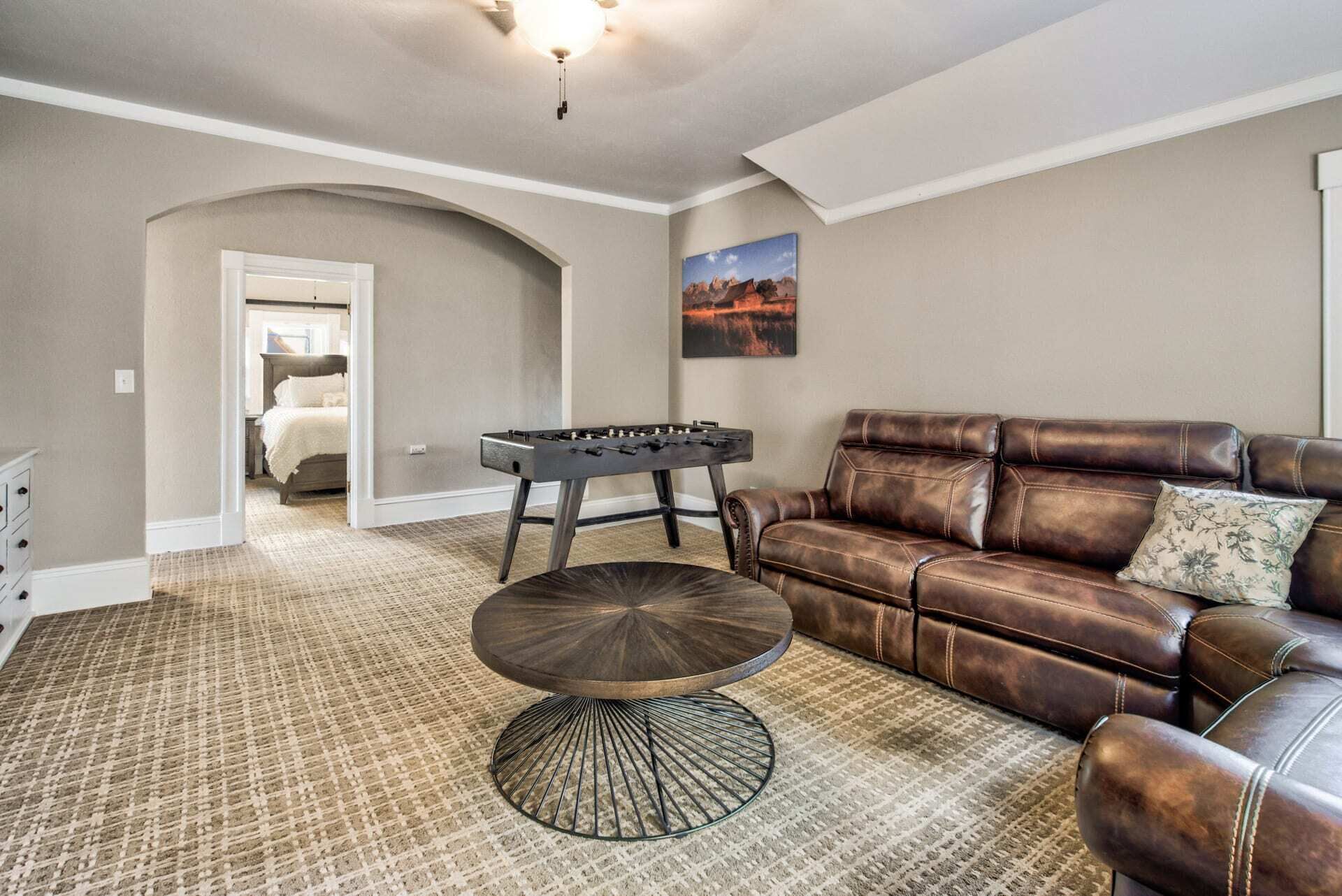 A living room with a brown leather sofa, a round coffee table, and a foosball table.
