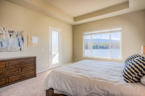 A bedroom with a large bed, a dresser, a door leading to a balcony, and a window with a view of a lake and mountains. - 5BD Lakeside Mountain Spectacularhot Tubluxury (Monument)