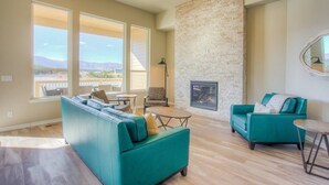 Un salon spacieux avec des canapés de couleur turquoise, une cheminée et de grandes fenêtres donnant sur l’extérieur.