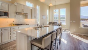 Une cuisine moderne avec des meubles blancs, un îlot central doté de tabourets et des luminaires suspendus.