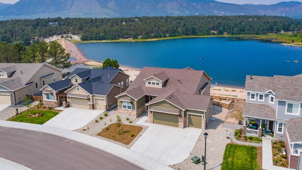 Un quartier résidentiel avec des maisons, une allée et un lac, avec des montagnes en arrière-plan.