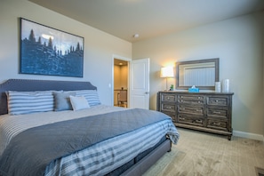 A bedroom with a large bed, a dresser, a painting, and a door leading to another room.