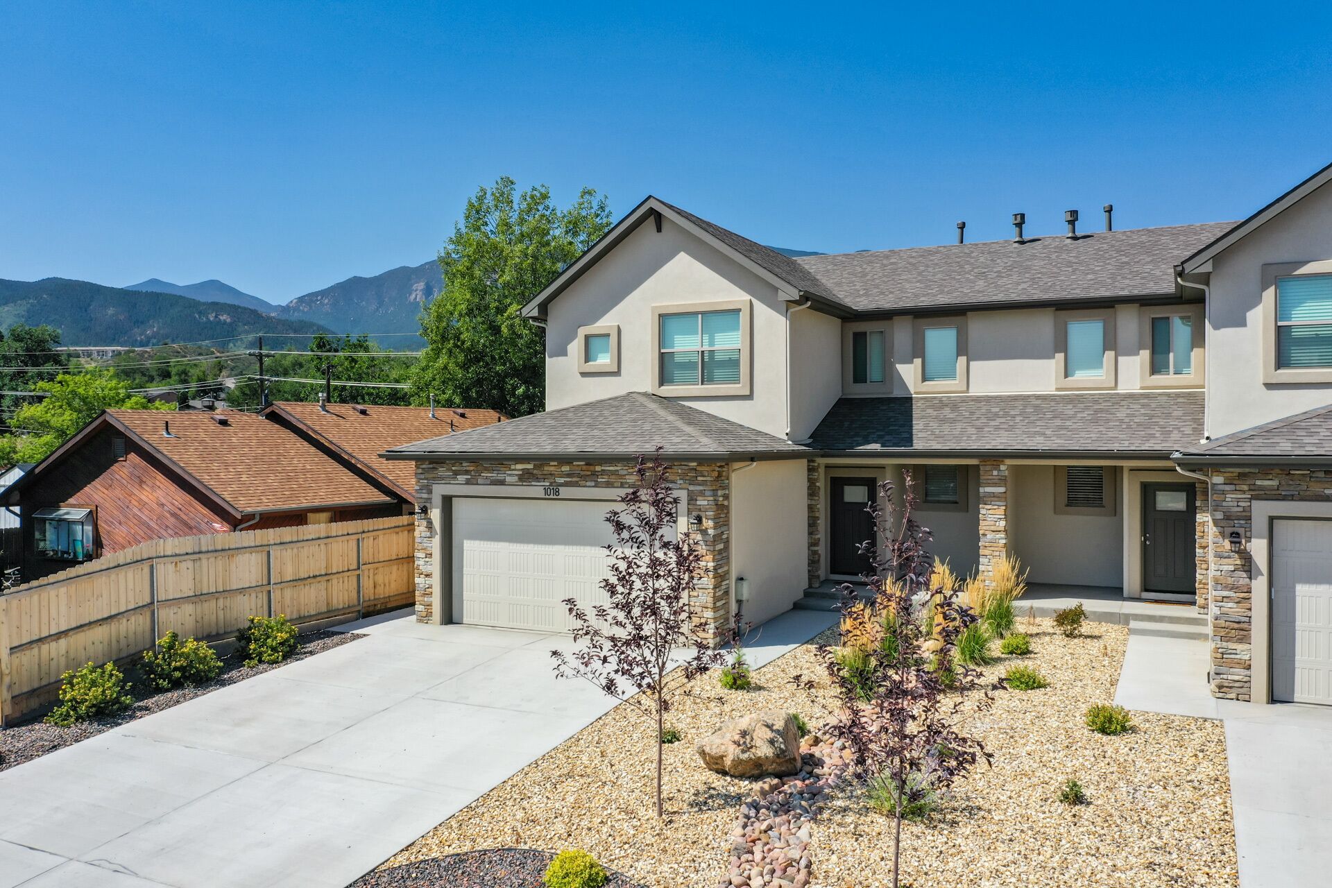 A two-story house with a stone facade, a garage, and a landscaped front yard with a small tree and decorative rocks.