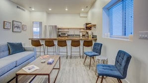 A modern living room with a sofa, a coffee table, and four bar stools. A kitchen with a refrigerator and a microwave is visible in the background. - 2bdmodern Garden Level-perfectoff Downtown Area (Colorado Springs)