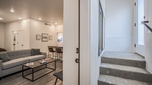 A modern living room with a grey sofa, a coffee table, and a dining area with two chairs. There are framed pictures on the wall and a staircase leading to another level. - 2bdmodern Garden Level-perfectoff Downtown Area (Colorado Springs)