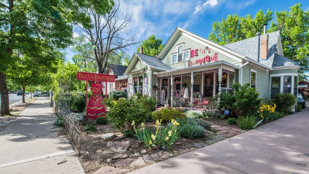 A boutique with a porch, surrounded by a garden with yellow flowers and a red sign. - 2BD Chic Cottage Mtns Walk Everywhere (Colorado Springs)