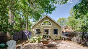 A small, single-story house with a gabled roof and a front porch. There is a garden area with a stone fountain, green chairs, and potted plants. - 2BD Chic Cottage Mtns Walk Everywhere (Colorado Springs)