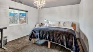 Ein Schlafzimmer mit Bett, Nachttisch, Lampe, einer Kristallleuchtreiter und einem Fenster mit Bergblick.