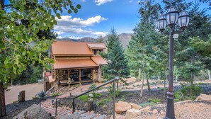 A two-story log cabin with a metal roof, surrounded by a landscaped garden with trees and a stone pathway leading to the entrance. - Mountain Getaway Cabinhot Tub & Pool Table4bd (Cascade)