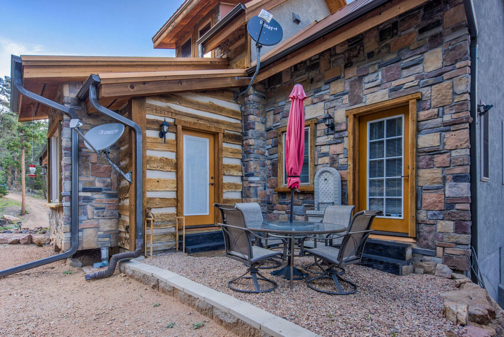 A stone building with a wooden porch, a glass table with chairs, and a satellite dish.