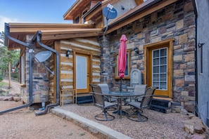 A stone building with a wooden porch, a glass table with chairs, and a satellite dish.