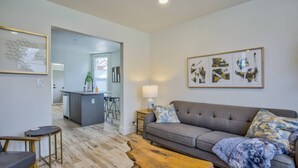 A modern living room with a grey sofa, wooden coffee table, and a kitchen area in the background. - 3BD Downtown Modern Victorian W/hot Tub, Park & Lake! (Colorado Springs)