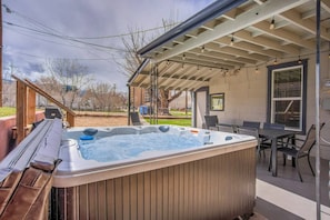 Ein Whirlpool in einem überdachten Außenbereich mit einer Holzterrasse und einem Tisch mit Stühlen in der Nähe.