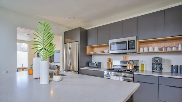 A modern kitchen with grey cabinets, a stainless steel refrigerator, a microwave, a gas stove, and a coffee maker. - 3BD Downtown Modern Victorian W/hot Tub, Park & Lake! (Colorado Springs)