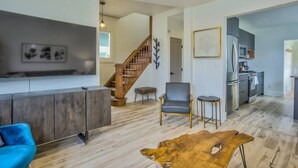 A modern living room with a wooden staircase, a grey armchair, a blue sofa, and a leather coffee table. - 3BD Downtown Modern Victorian W/hot Tub, Park & Lake! (Colorado Springs)