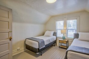 Ein Schlafzimmer mit zwei Betten, einem Fenster mit Jalousien, einem Nachttisch mit Lampe und einer Tür.