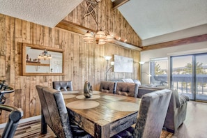 Enjoy meals in this dining area with a large table and comfortable chairs, surrounded by a high ceiling and a large window offering a view of the outdoors.