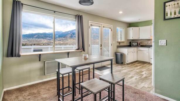 Una cocina moderna con comedor, ventanas grandes con cortinas y vistas a montañas.