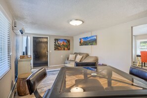A modern living room with a glass-top coffee table, a sofa, and two paintings on the wall.