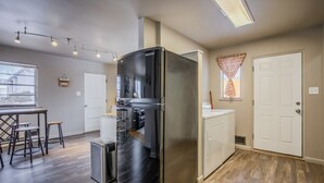 Uma cozinha com geladeira de aço inoxidável, uma pequena ilha com banquetas e uma janela com vista para o exterior.