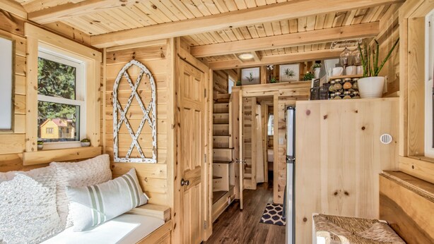 L’intérieur d’une cabane en bois, avec un lit, une fenêtre, un escalier et un petit coin salon.