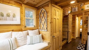 L’intérieur d’un chalet en bois, avec un lit confortable, une porte à arc décorative et une fenêtre donnant sur les arbres.