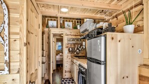 Une petite cabane en bois comprenant un coin cuisine équipé d’un réfrigérateur, d’une cuisinière et de placards en bois.