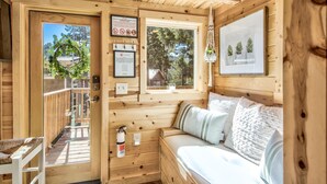 L’intérieur d’un chalet en bois, avec un lit, une porte donnant sur l’extérieur et une fenêtre offrant une vue sur les arbres.