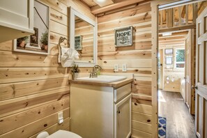 Bagno di una baita in legno con lavandino, specchio e un cartello con su scritto: 'Questa speranza è un'ancora per l'anima'.