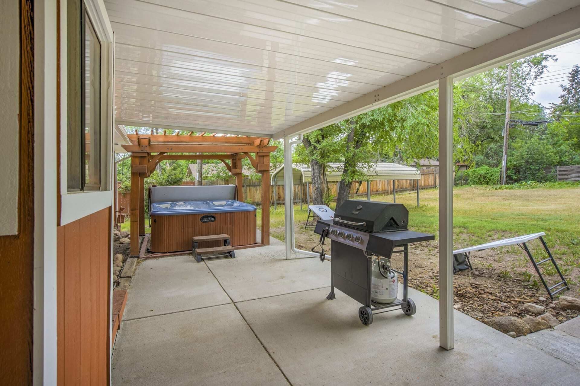 Un patio exterior con un jacuzzi, una parrilla y una pérgola.