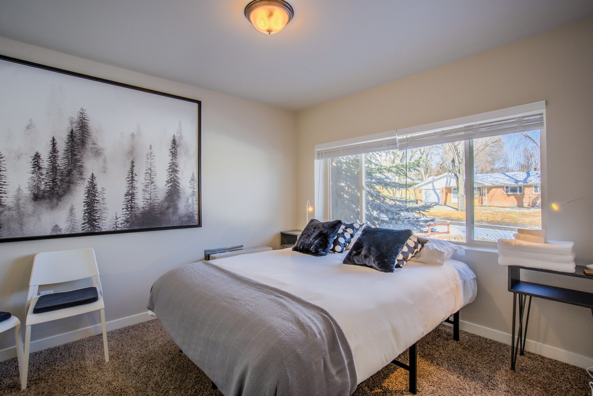 A bedroom with a bed, a chair, a desk, a window with a view of the outside, and a painting on the wall.