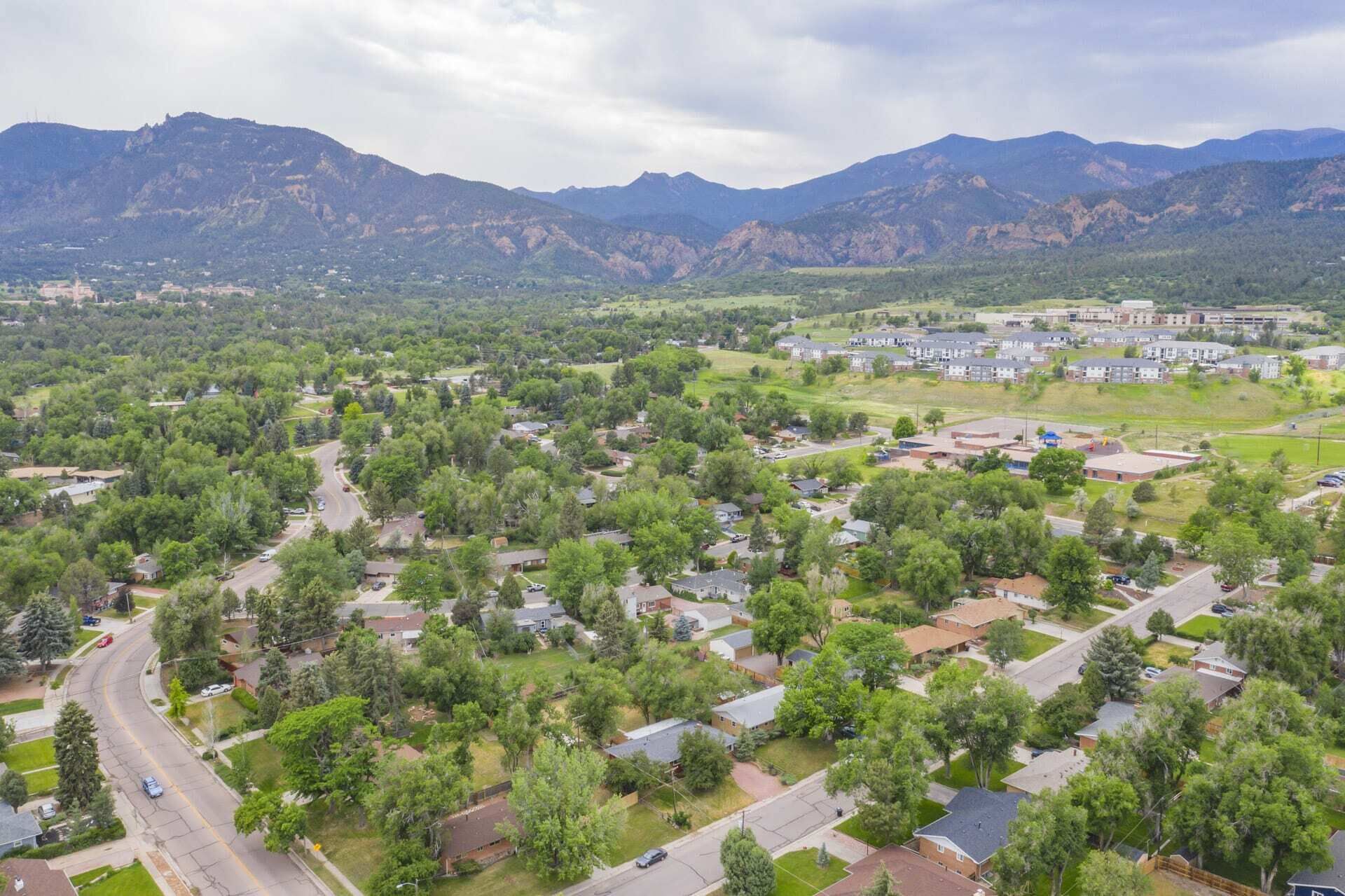 An aerial view of a residential area with houses, roads, and a large building complex in the background.