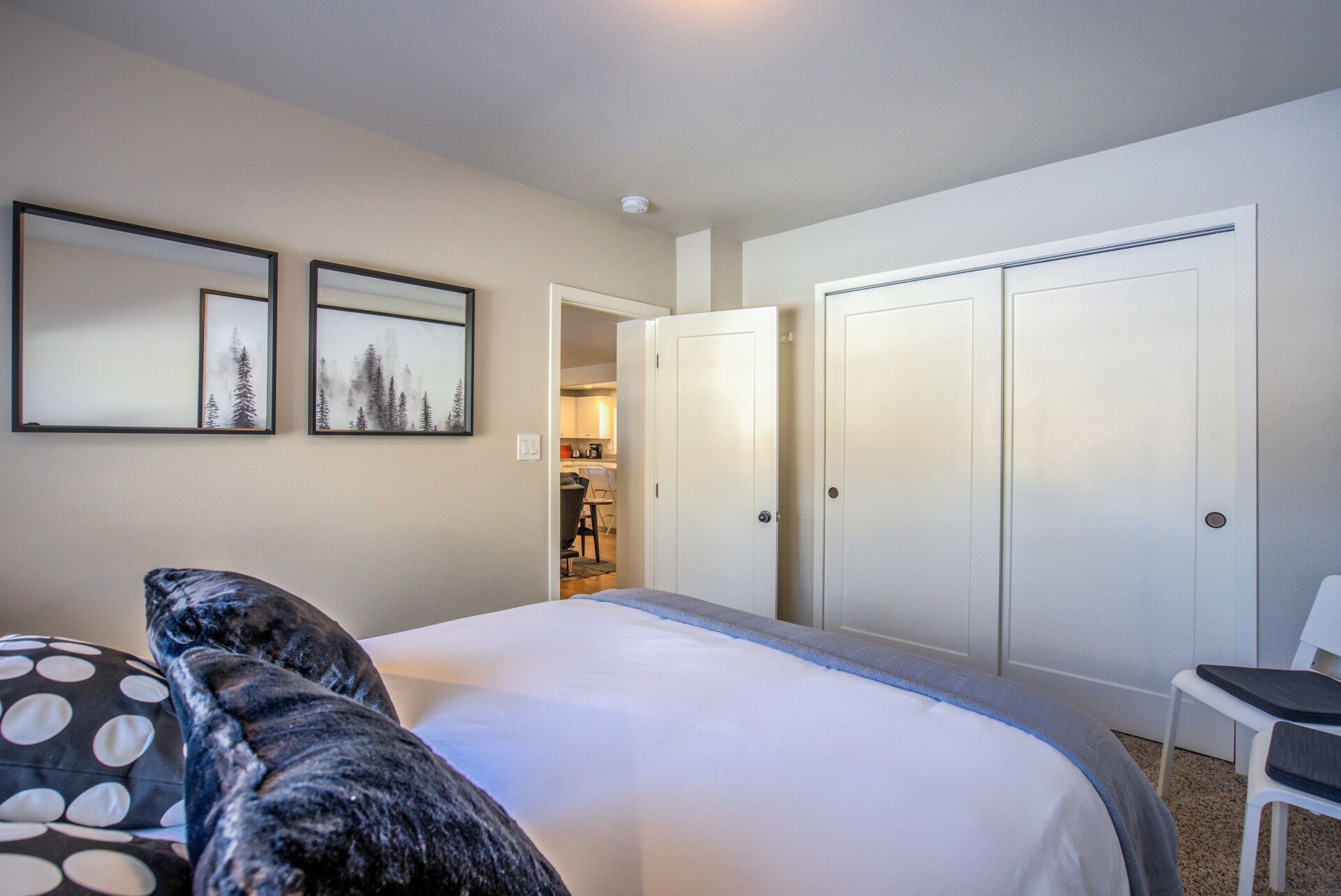 A hotel room with a bed, two framed pictures on the wall, a chair, and a wardrobe.