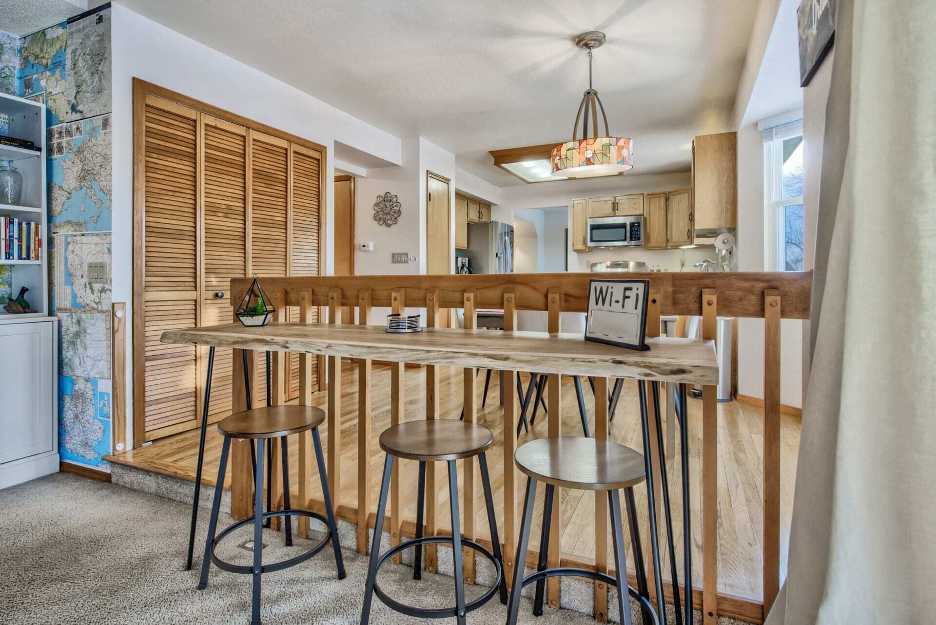 Une cuisine avec un banc et des tabourets en bois, un panneau indiquant la présence d’une connexion Wi-Fi et une carte accrochée au mur.