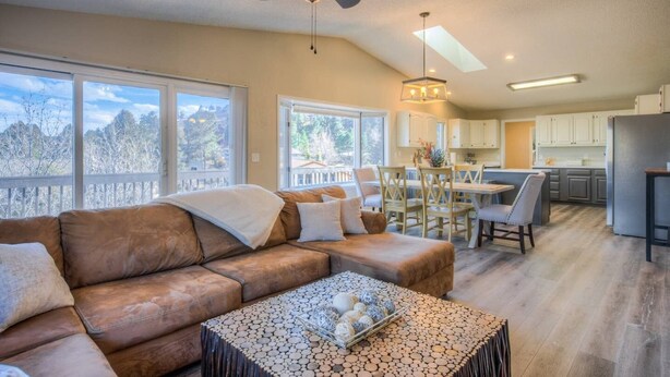 A spacious living room with a brown leather sofa, a dining area with wooden chairs, a kitchen with white cabinets, and a ceiling fan.