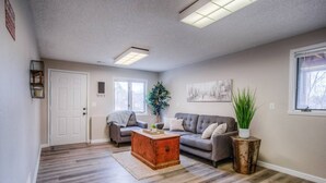 A spacious living room with hardwood flooring, a grey sofa, a wooden coffee table, and a potted plant.