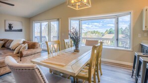 A spacious living room with a large sofa, a dining table with chairs, and a view of the outdoors through large windows.