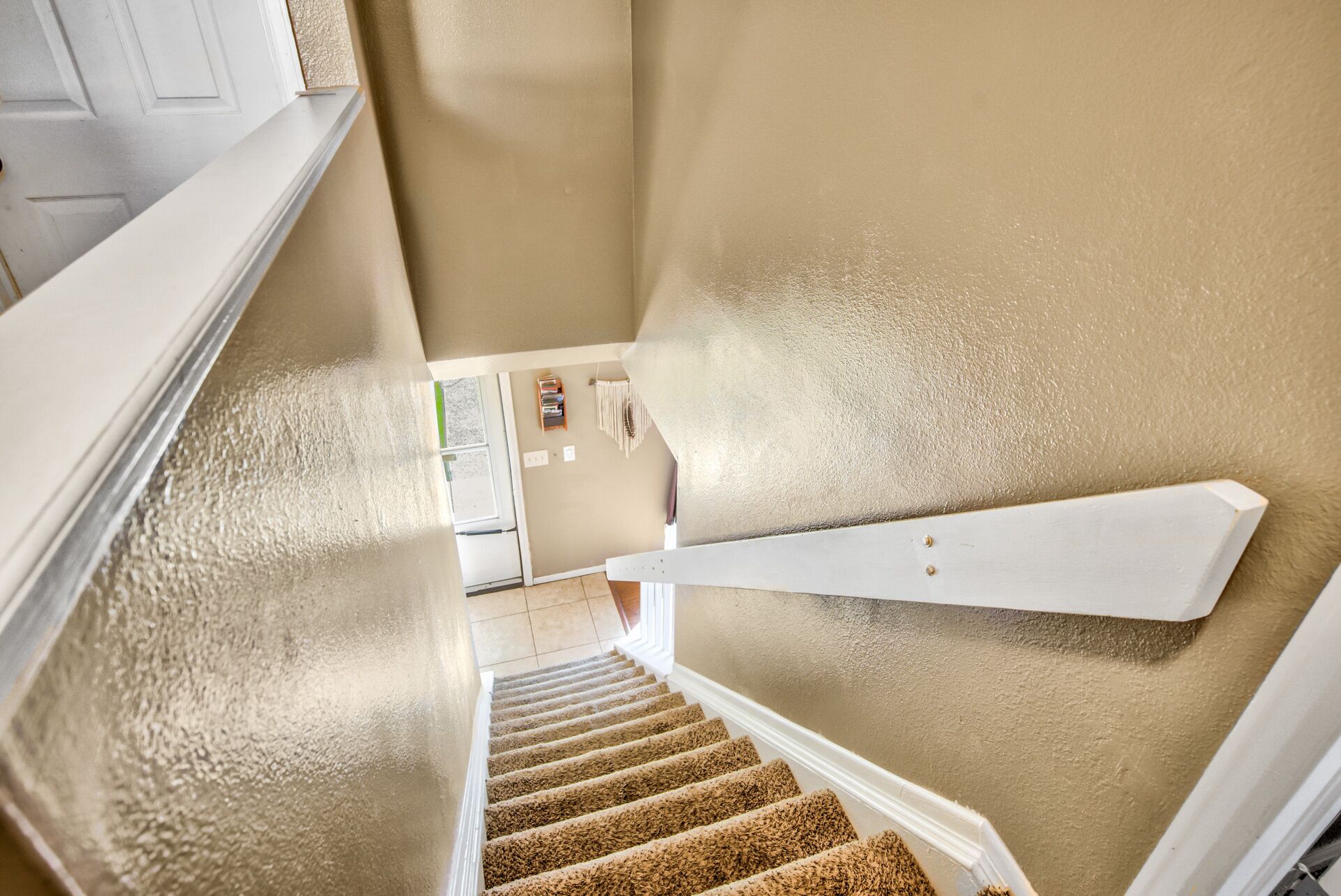 A staircase with beige walls and white trim, leading to a landing with a door and a small shelf with books.